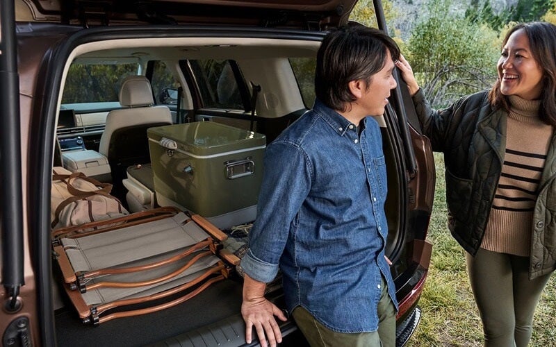 A couple talking by the trunk of a Hyundai Santa Fe while unloading items in a wooded area
